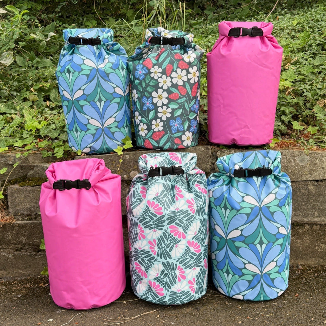6 colorful, patterned dry bags on a rock wall with grass behind them