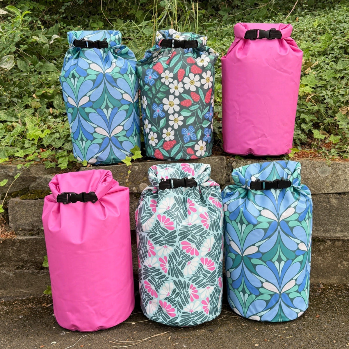 6 colorful, patterned dry bags on a rock wall with grass behind them