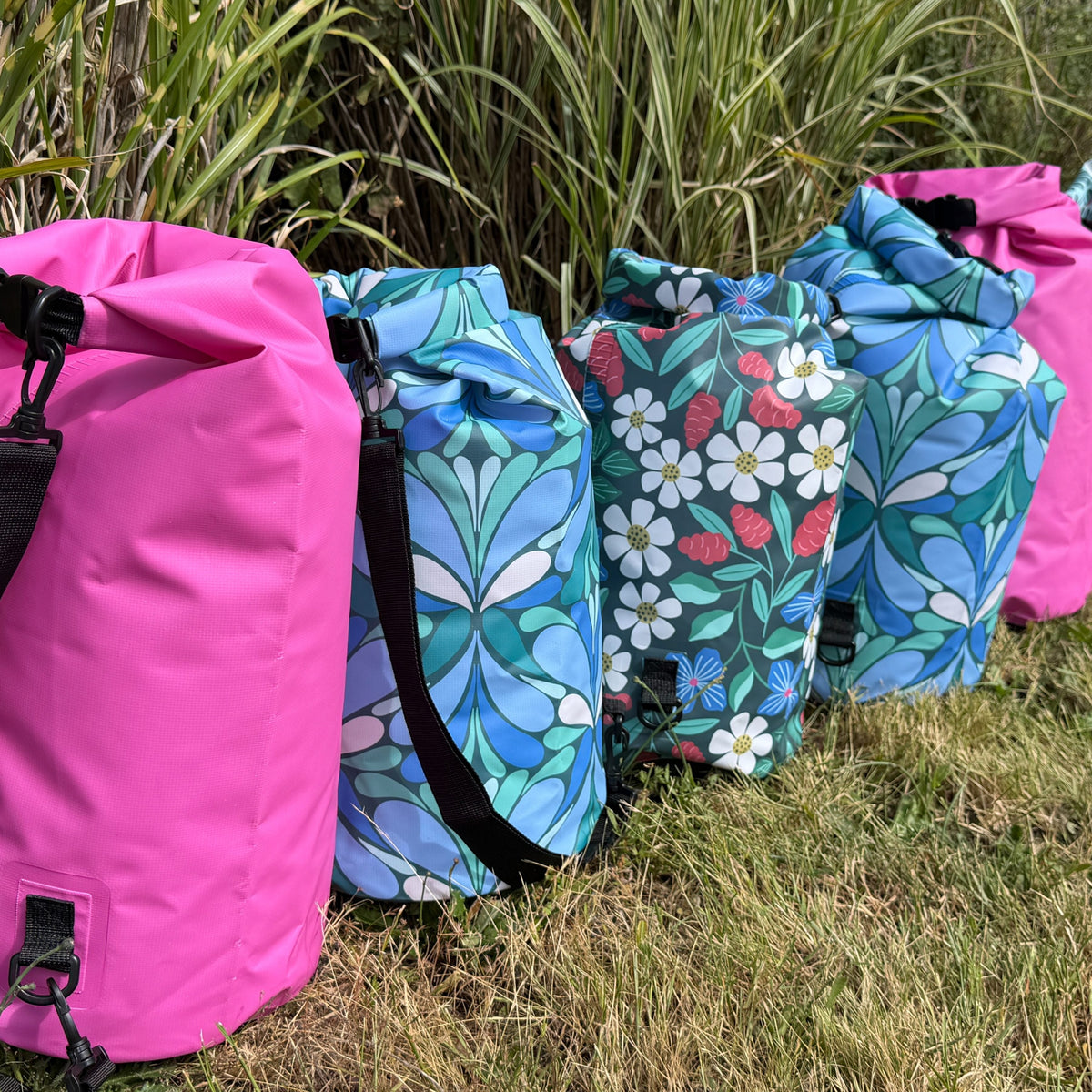 Row of 5 colorful, patterned dry bags on grass