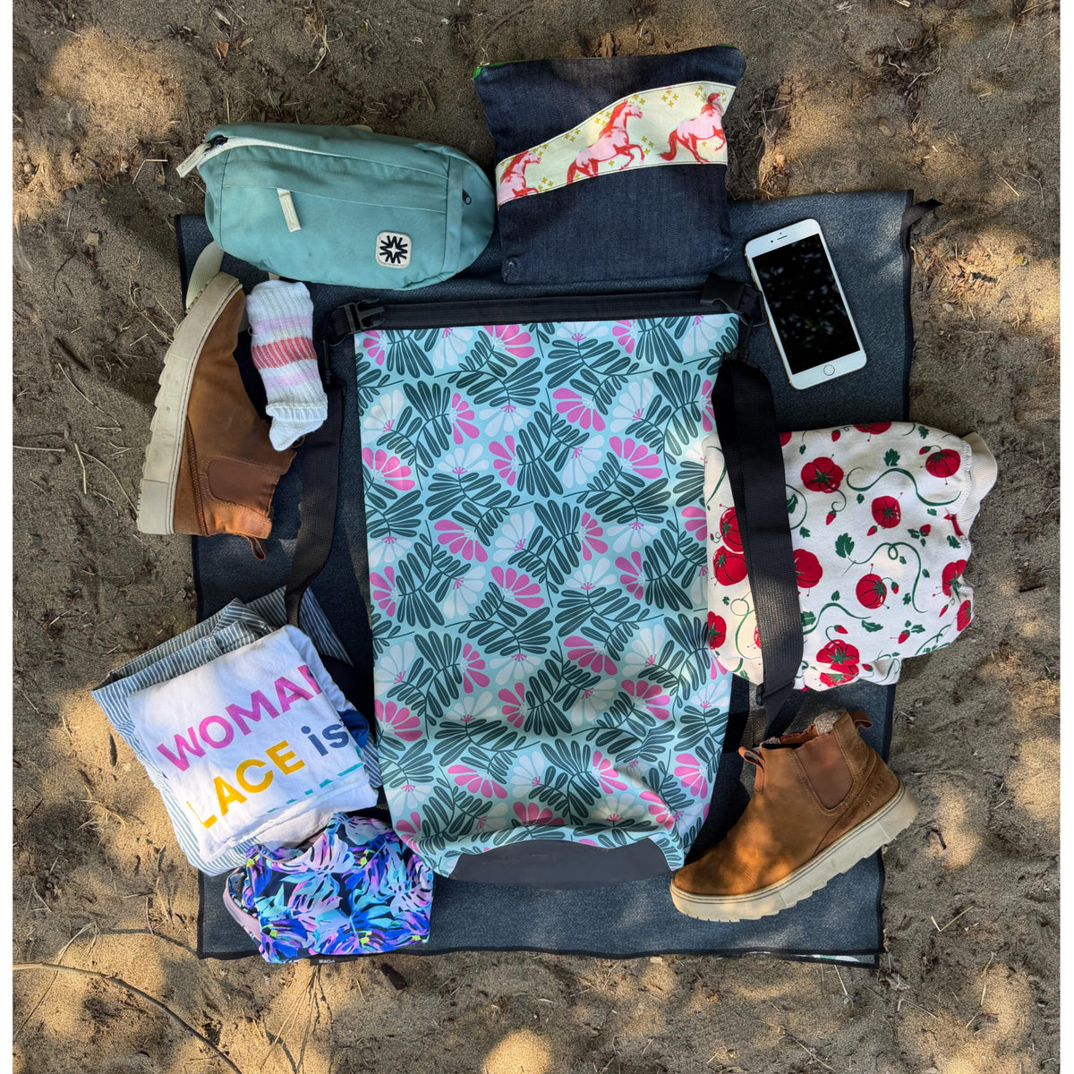 A bunch of items to pack in a colorful patterned dry bag on the sand