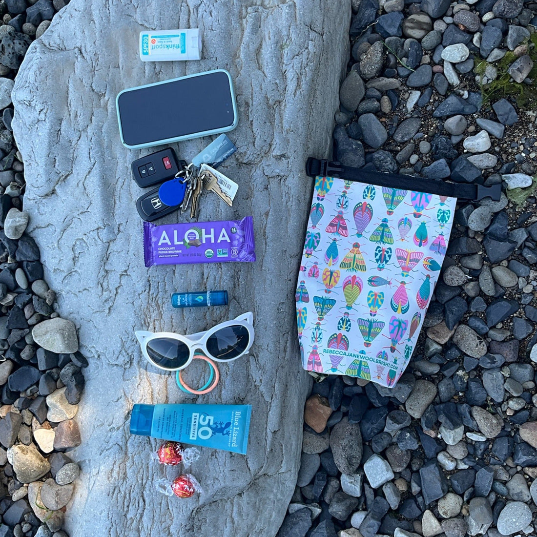 A group of small items on a log sitting next to a 2L dry bag with a moth pattern