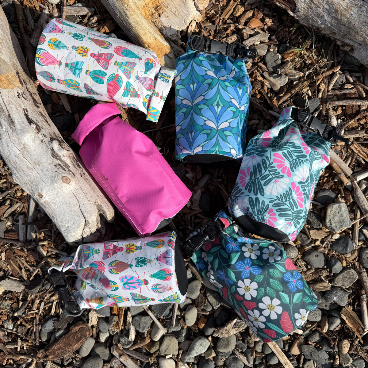 six colorful dry bags on river rocks