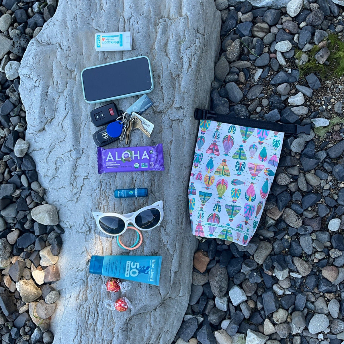 small dry bag with sunscreen and other small items laid next to it on rocks