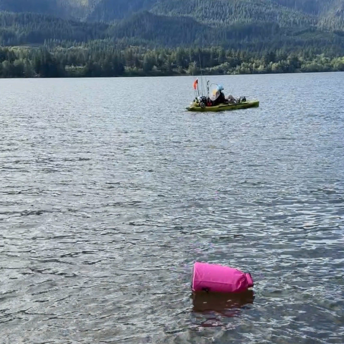 Floating pink dry bag on the water next to a kayak