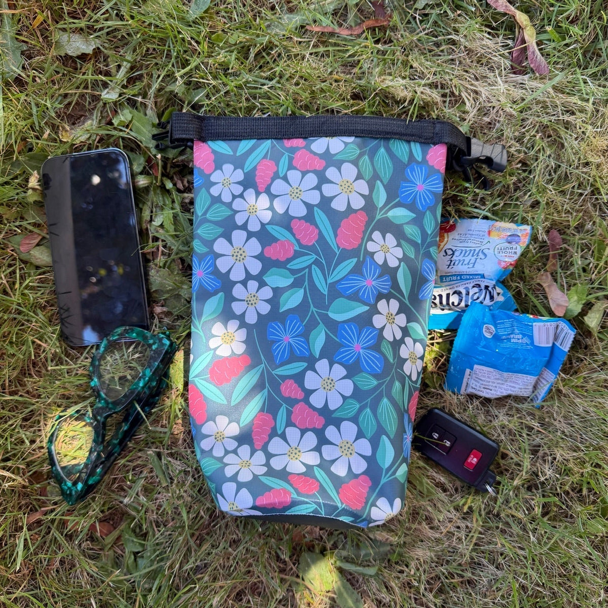 Floral dry bag with items spread around it on grass