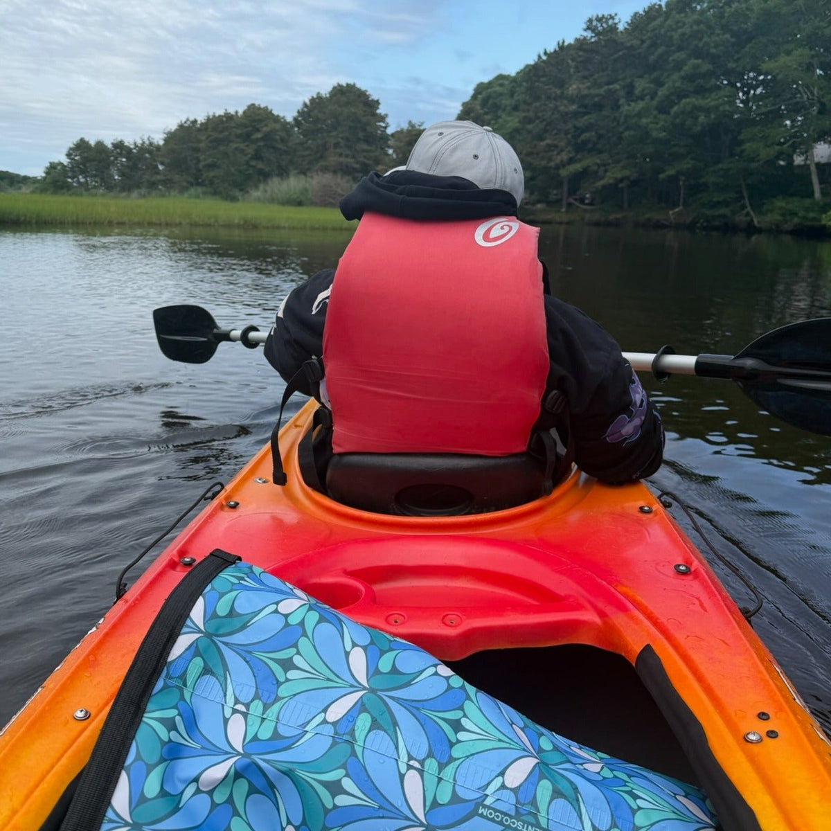 Kayaker in red vest on orange kayak with colorful patterned dry bag