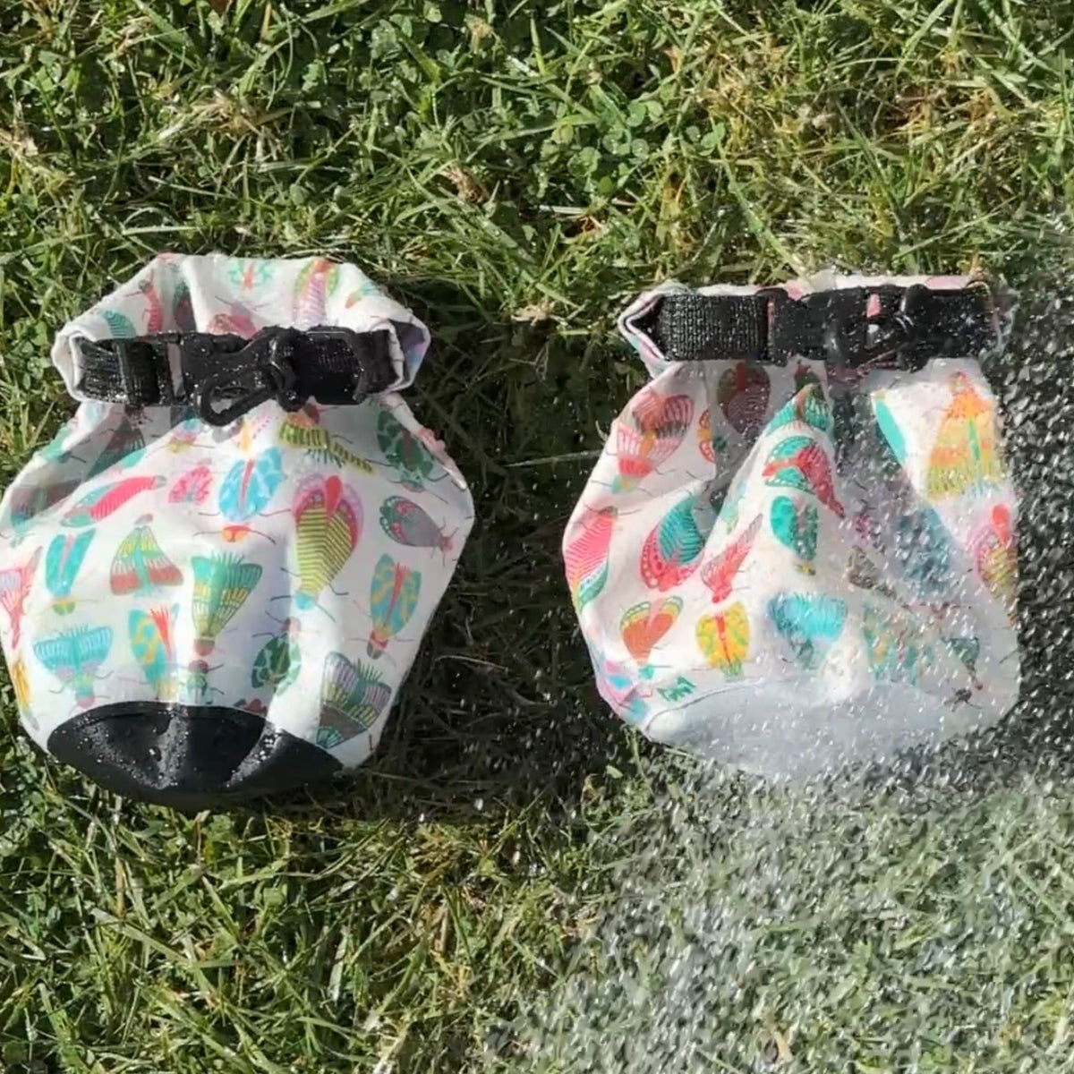 Two colorful moth dry bags being sprayed by water on grass