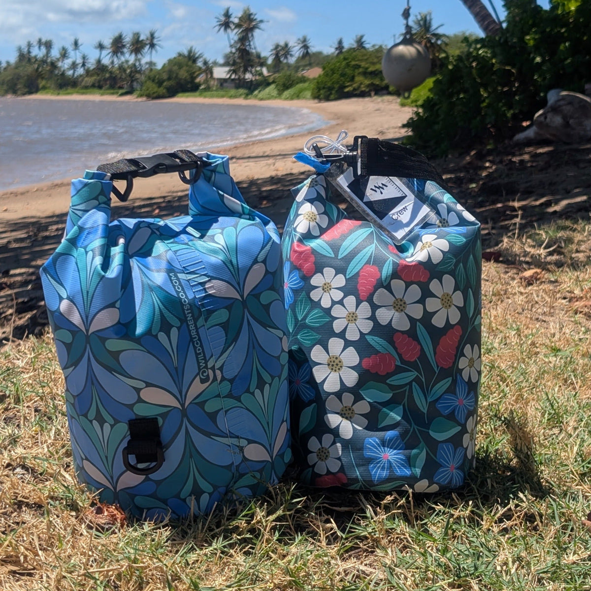 Two Colorful, patterned dry bags on grass with the ocean in the background