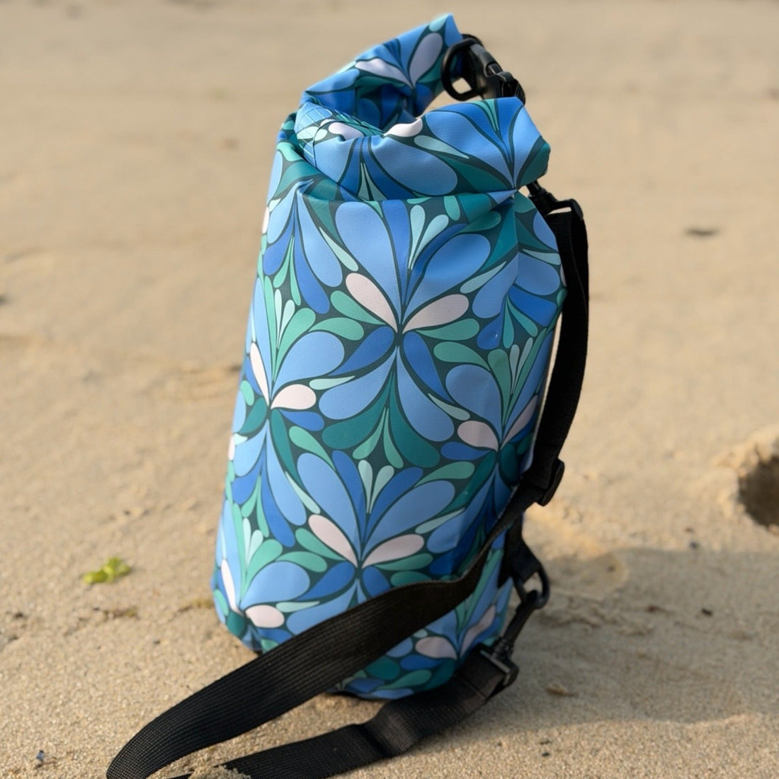 Blue patterned dry bag on beach with backpack straps
