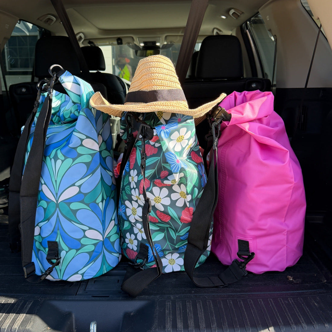 Three colorful dry bag backpacks in the back of a car with a hat on top