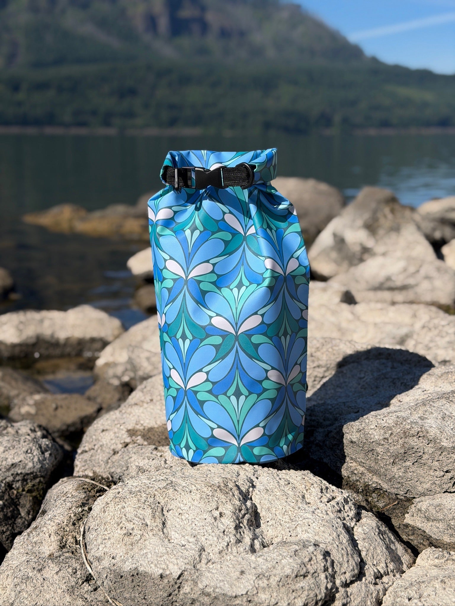 blue and green geometric print dry bag on rocks by a river