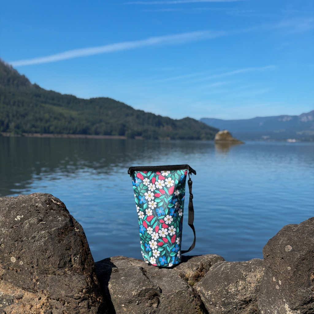 The 10L floral print dry bag on a rocky shoreline showing the black removable shoulder strap attached to the side.