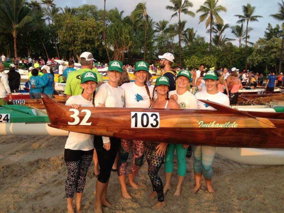 Womens crew standing behind a koa canoe at the Queen Lilio race on the beach on Kona.