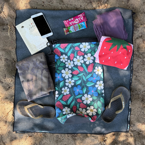 The image shows 10 liter dry bag a floral roll-top dry bag from Wild Currents Co. laid out on a blanket with beach and travel accessories.