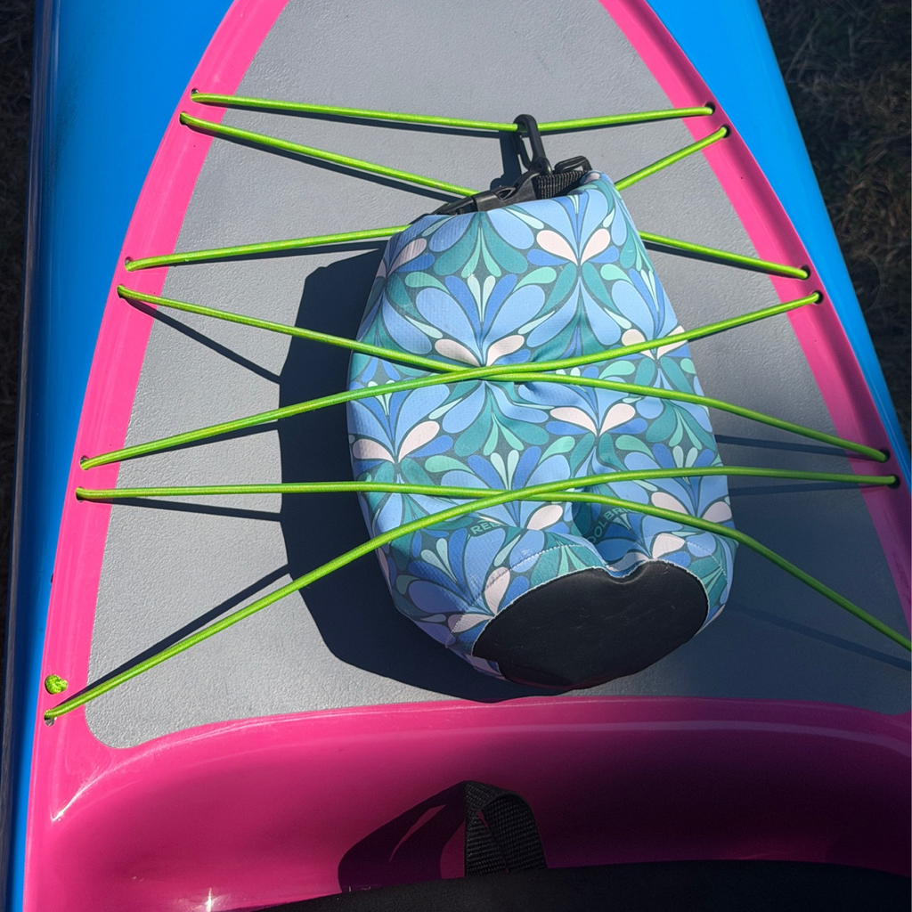 The image shows a blue paisley patterned Yuba 2L Waterproof Dry Bag secured under the bungee deck rigging of a stand-up paddleboard.