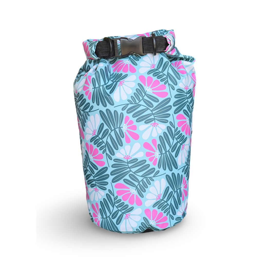 The Napili 10L waterproof dry bag featuring a tropical pattern of dark green palm leaves, bright pink flowers, and light blue accents, standing upright against a clean white background.