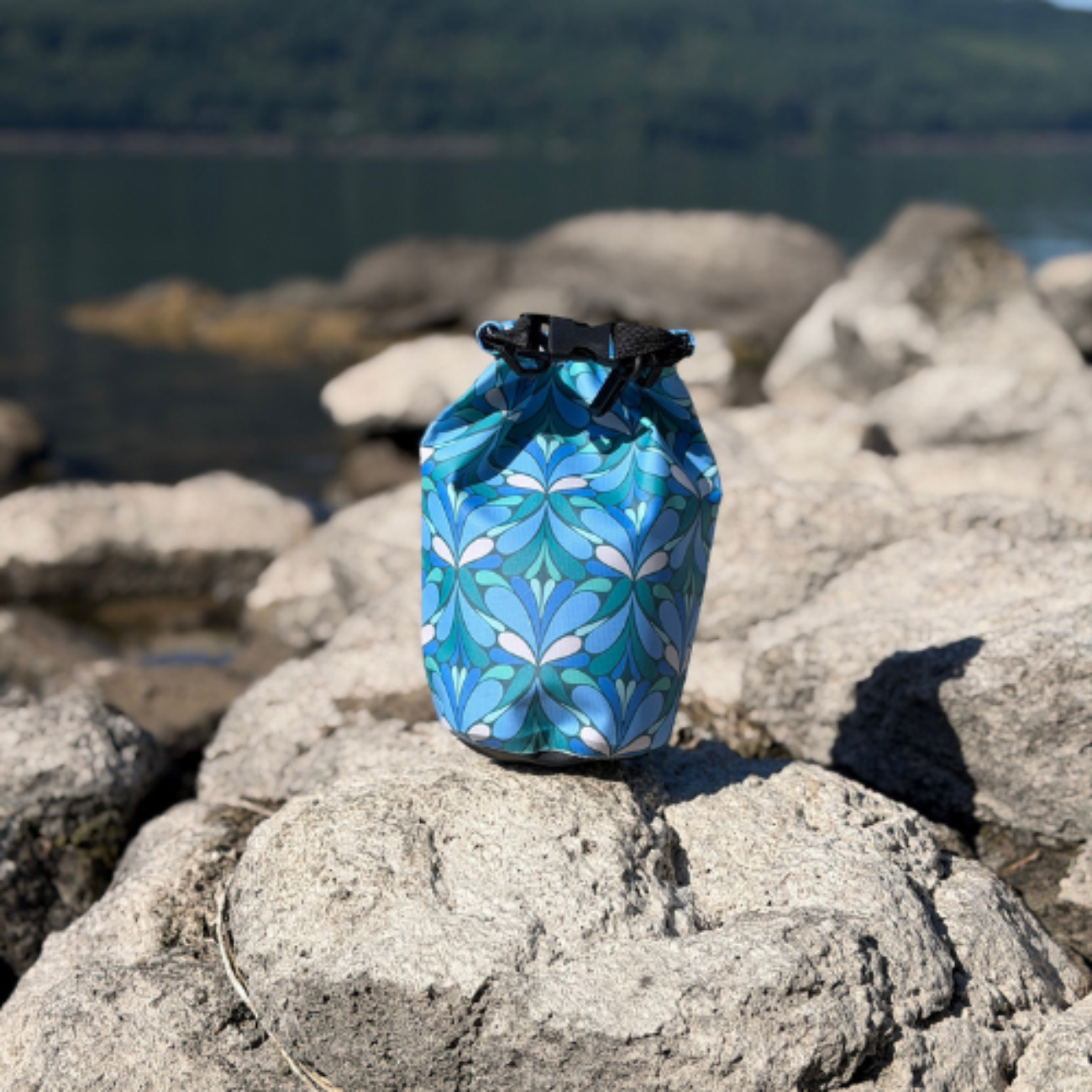 Blue patterned drawstring bag on a rock with a lake and mountains in the background