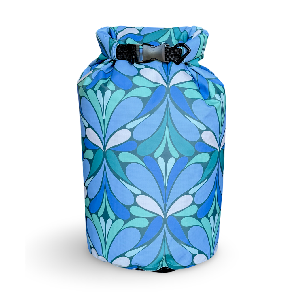 The Yuba 20L waterproof dry bag with a vibrant blue, teal, and aqua geometric petal pattern, standing upright on a white background with its roll-top closure buckled.